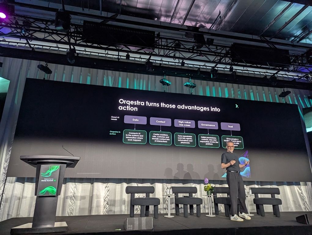 Chris Smith on stage with a slide reading "Orqestra turns those advantages into action"